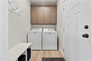 Washroom featuring separate washer and dryer, light wood-type flooring, and cabinet space