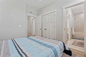 Bedroom featuring a closet, ensuite bath, and light wood-style flooring