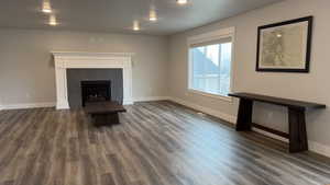 Unfurnished living room with a warm lit fireplace and dark wood-type flooring