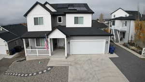View of front facade with roof with shingles, solar panels, driveway, and covered porch