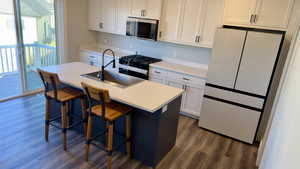 Kitchen with freestanding refrigerator, a kitchen island with sink, white cabinetry, and gas stove