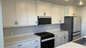 Kitchen featuring black gas stove, light countertops, white cabinets, and freestanding refrigerator