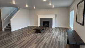 Unfurnished living room featuring stairs, dark wood finished floors, and a fireplace