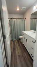 Full bathroom with curtained shower, vanity, and dark wood-style floors