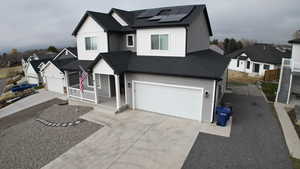 View of front of property featuring roof with shingles, a porch, driveway, and roof mounted solar panels