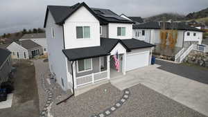 View of front of house with concrete driveway, roof with shingles, a porch, a garage, and roof mounted solar panels