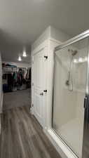 Bathroom featuring a walk in closet, a shower stall, and dark wood-style flooring