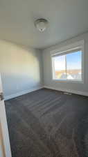 Spare room featuring dark colored carpet and baseboards