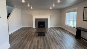 Unfurnished living room with stairs, dark wood-style flooring, and a lit fireplace