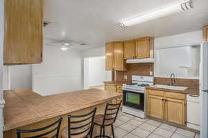 Kitchen with a breakfast bar, white appliances, a peninsula, light tile patterned flooring, and a textured ceiling