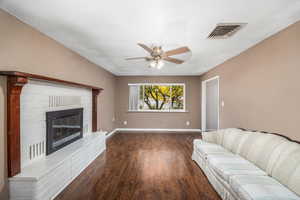 Living area with a fireplace, dark wood-style floors, ceiling fan, and a textured ceiling