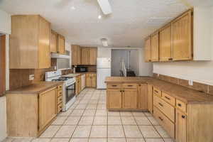 Kitchen featuring white appliances, a peninsula, a textured ceiling, light tile patterned floors, and tile countertops