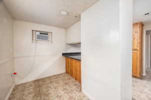 Kitchen with a textured ceiling, light tile patterned flooring, dark stone countertops, and a wall mounted AC