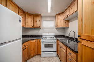 Kitchen with white appliances, dark stone countertops, light tile patterned floors, brown cabinets, and a textured ceiling