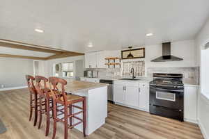 Kitchen with stainless steel appliances, white cabinetry, light countertops, a kitchen bar, and wall chimney exhaust hood