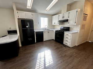 Kitchen featuring light countertops, white cabinetry, black appliances, a heating unit, and vaulted ceiling