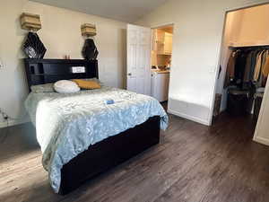 Bedroom with a walk in closet, dark wood finished floors, washer and dryer, and vaulted ceiling