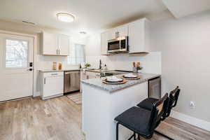 Kitchen with a peninsula, light stone countertops, white cabinetry, and light wood finished floors