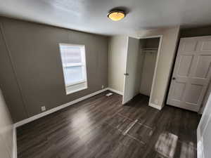 Unfurnished bedroom with a closet, dark wood-style floors, and a textured ceiling