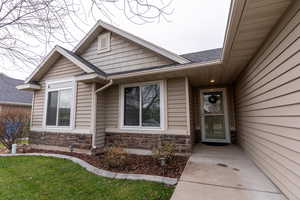Doorway to property featuring stone siding, a lawn, and a shingled roof