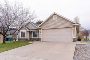 View of front facade featuring stone siding, concrete driveway, a front yard, and a garage