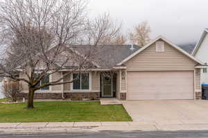 View of front of house featuring stone siding, a front yard, driveway, and a garage