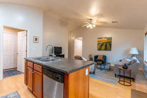 Kitchen featuring an island with sink, open floor plan, stained cabinetry, vaulted ceiling, and dishwasher