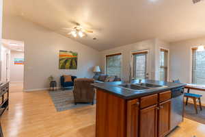 Kitchen featuring a kitchen island with sink, light wood finished floors, dark countertops, ceiling fan, and dishwasher