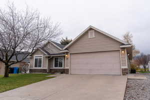 View of front of property featuring stone siding, driveway, a front lawn, and attached garage