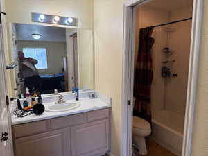 Ensuite bathroom with vanity, shower / bathtub combination with curtain, a textured ceiling, and a textured wall