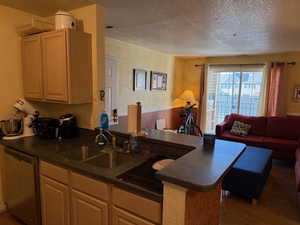 Kitchen with dark countertops, open floor plan, stainless steel dishwasher, a textured ceiling, and a peninsula