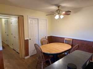 Dining area with dark wood-style floors, a textured ceiling, a ceiling fan, and wainscoting