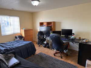 Bedroom with a desk, light wood finished floors, and a textured ceiling