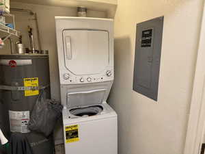 Washroom with electric panel, stacked washer / dryer, strapped water heater, and a textured wall