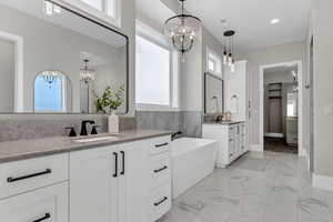 Bathroom with a spacious closet, two vanities, a chandelier, a freestanding tub, and healthy amount of natural light