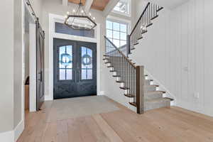 Entryway featuring a barn door, light wood-style floors, beamed ceiling, french doors, and a high ceiling