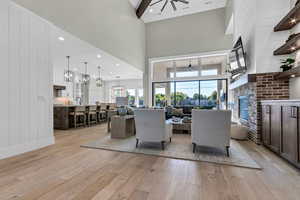 Living room featuring a stone fireplace, light wood-style floors, a chandelier, ceiling fan, and wood walls