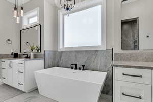 Full bath featuring a freestanding bath, tile walls, marble look tile flooring, vanity, and wainscoting