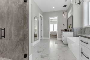 Full bath with ensuite bathroom, vanity, light marble finish flooring, a freestanding bath, and a marble finish shower