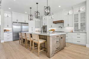 Kitchen featuring glass insert cabinets, white cabinets, stainless steel appliances, backsplash, and decorative light fixtures