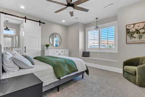 Carpeted bedroom with a barn door and a ceiling fan