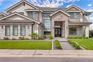 View of front of property with a front lawn, stone siding, stucco siding, and french doors