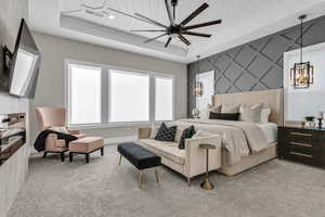 Bedroom featuring an accent wall, a tray ceiling, carpet floors, and ceiling fan