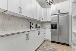 Kitchen with stainless steel refrigerator with ice dispenser, white cabinetry, light stone counters, tasteful backsplash, and a chandelier
