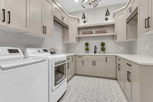 Washroom featuring washer and clothes dryer, cabinet space, and a chandelier