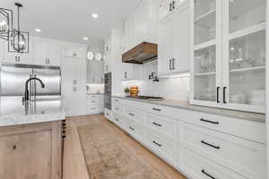 Kitchen with glass insert cabinets, decorative light fixtures, light stone counters, appliances with stainless steel finishes, and white cabinetry
