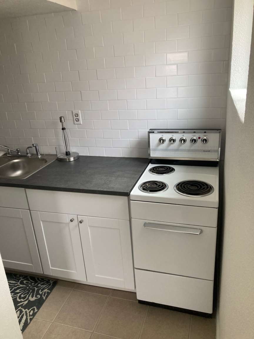 Compact kitchen featuring a white electric range, dark countertop, and stainless steel sink