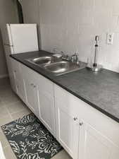 Kitchen featuring white cabinetry, dark countertops, light tile patterned floors, and freestanding refrigerator
