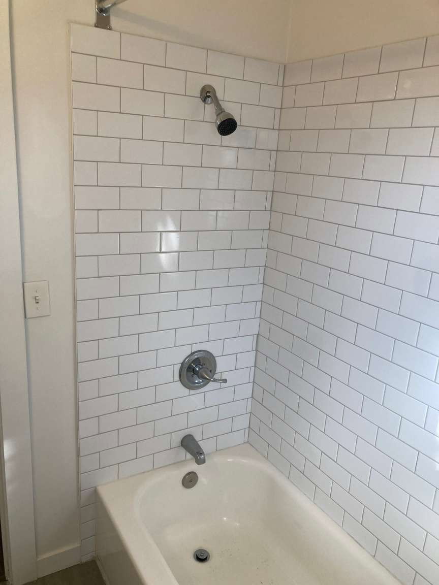 Bathtub and shower combination featuring subway tile surround, polished chrome showerhead, and matching tub spout with control handle