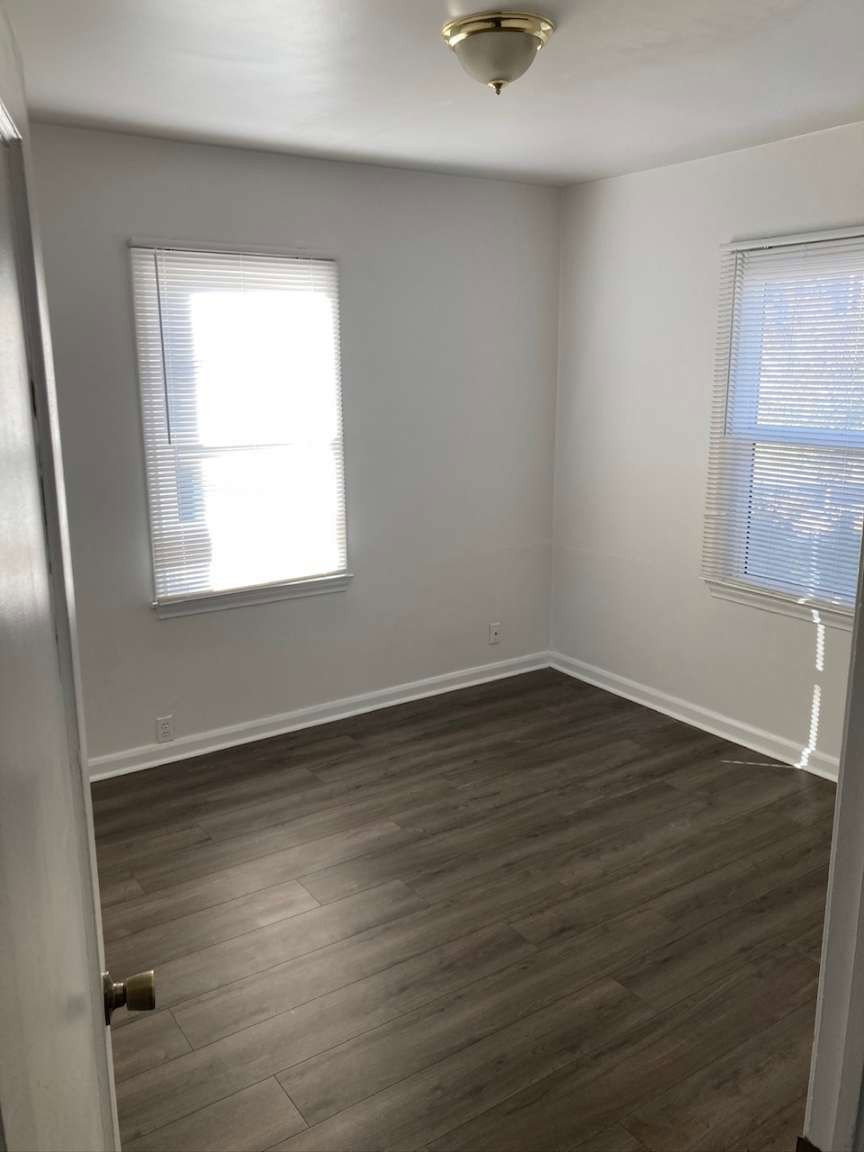 Room featuring neutral white walls, two windows with horizontal blinds, and wood-finish flooring